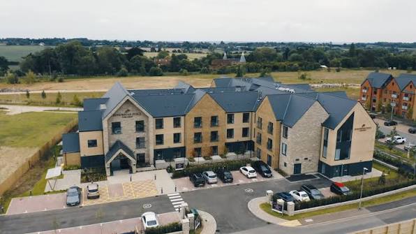 Rose Water Place Care Home large brick building with numerous windows. Car park and surrounding greenery.