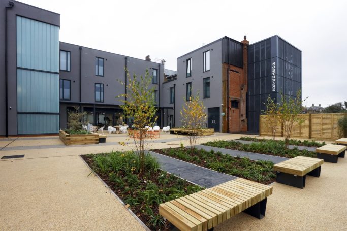 Modern building with landscaped gardens, wooden benches, and decorative trees.