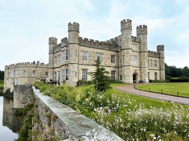 Historic stone castle with multiple towers, surrounded by greenery and a moat.