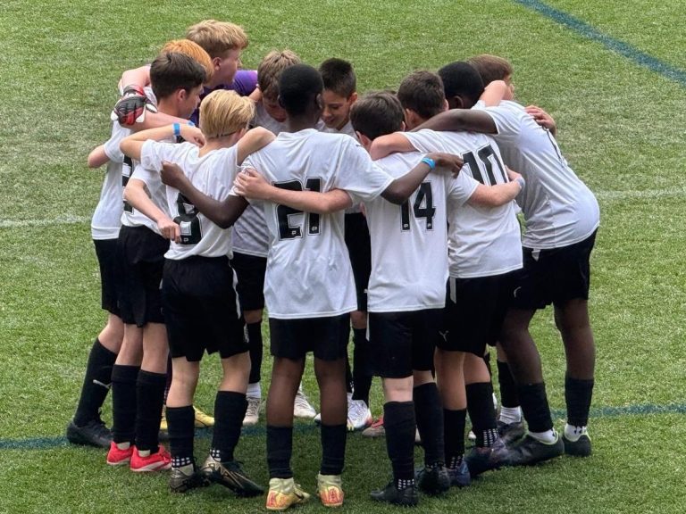 Dartford Under 13s Team Group of children in a huddle wearing football kit on grass field