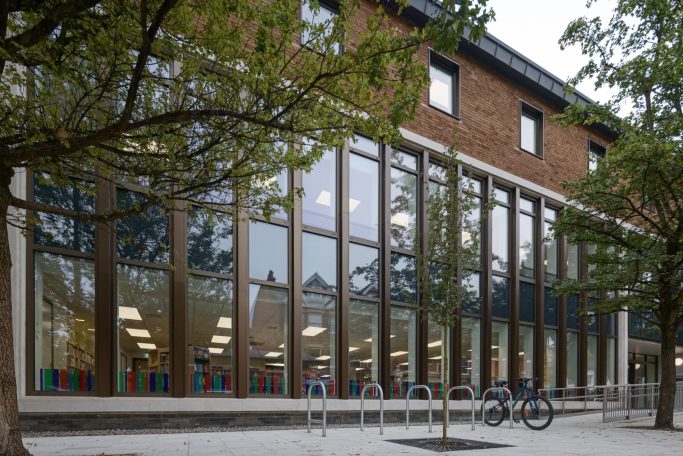 Modern building with large windows, trees, and bicycle outside.